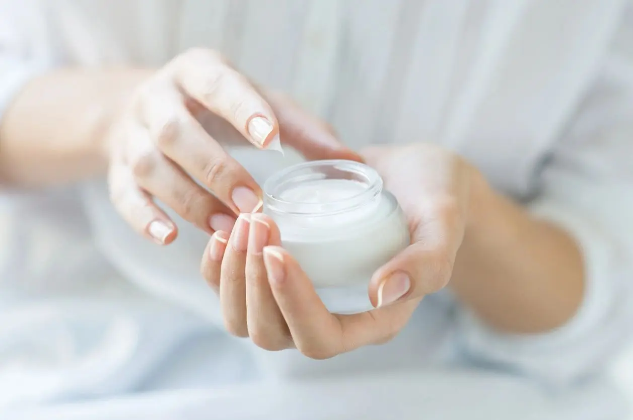 A person holding a jar of cream in their hands.