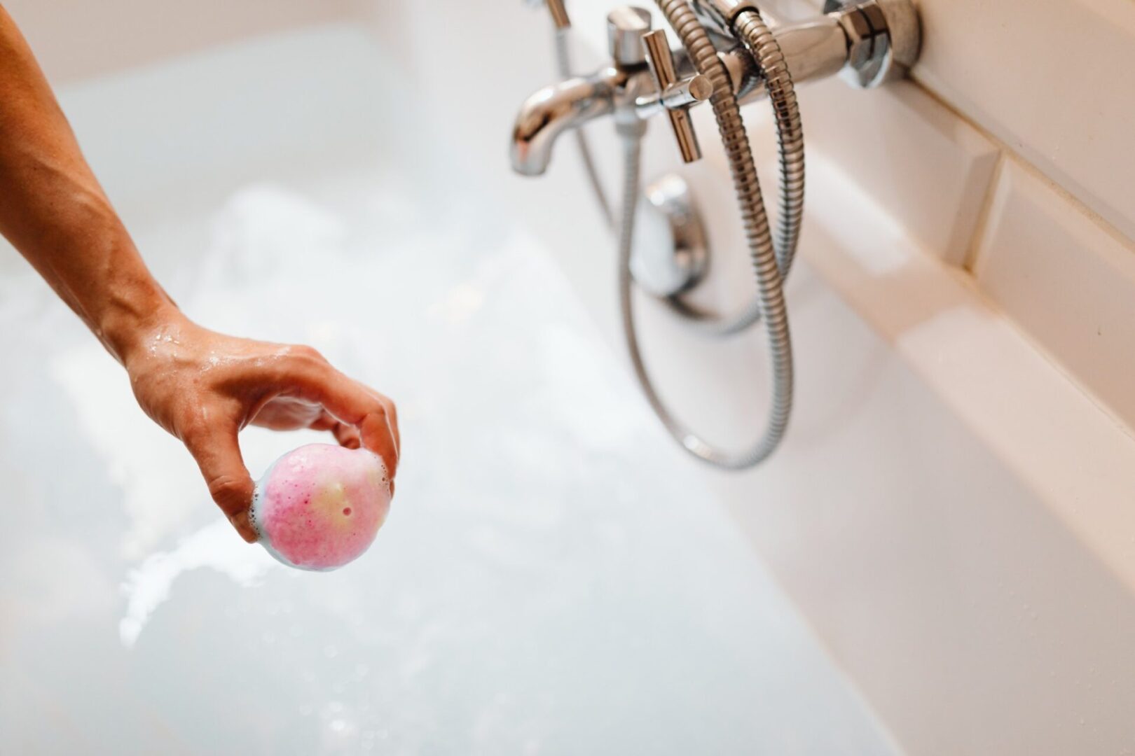 A person holding an object in front of the bathtub.